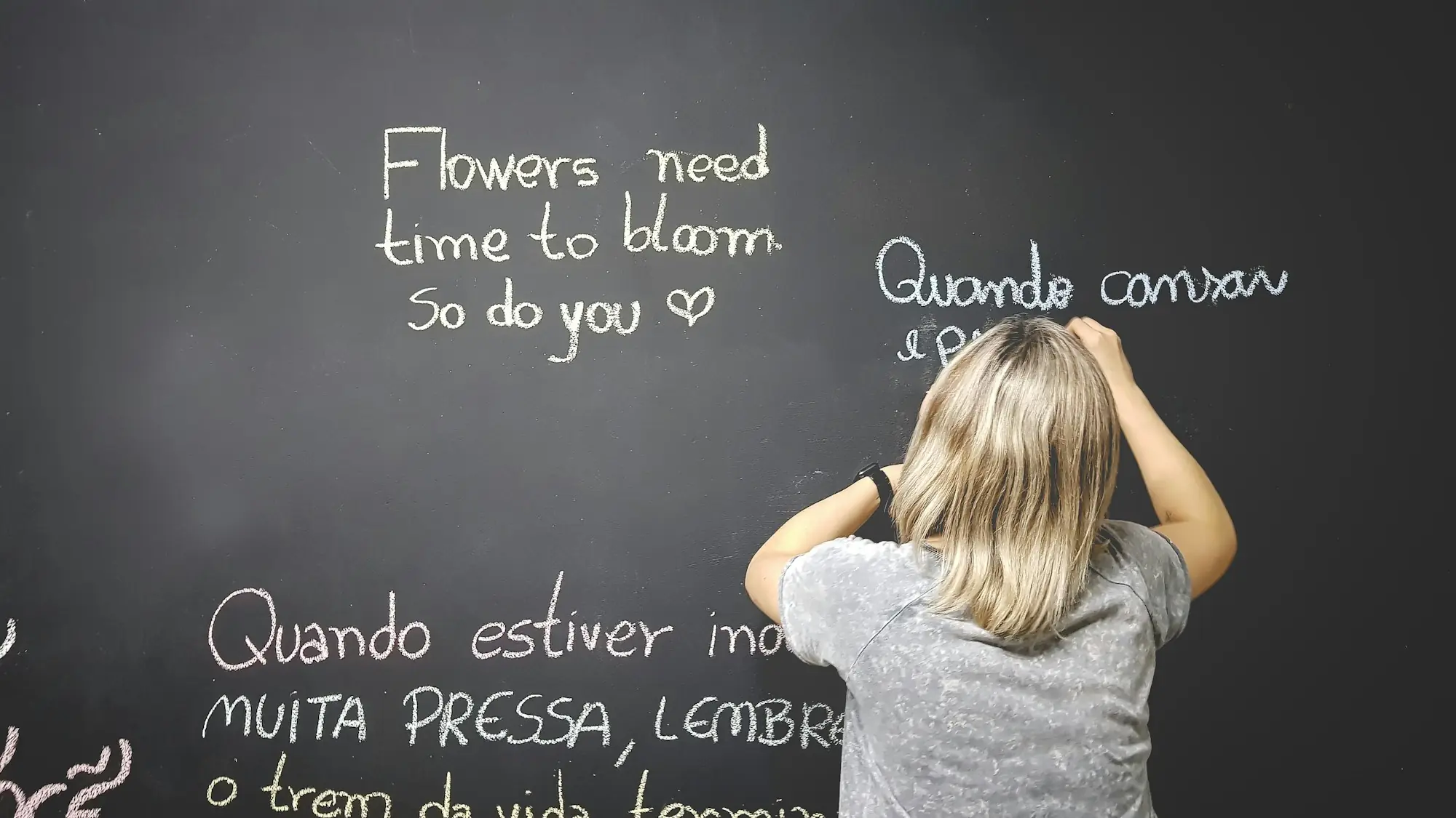 Pessoa escrevendo frases em inglês e português em um quadro-negro